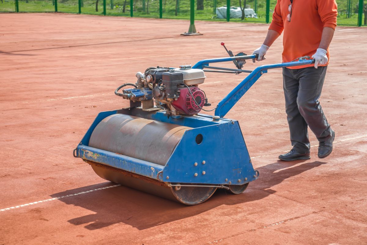 A man using rollers to flatten the court.