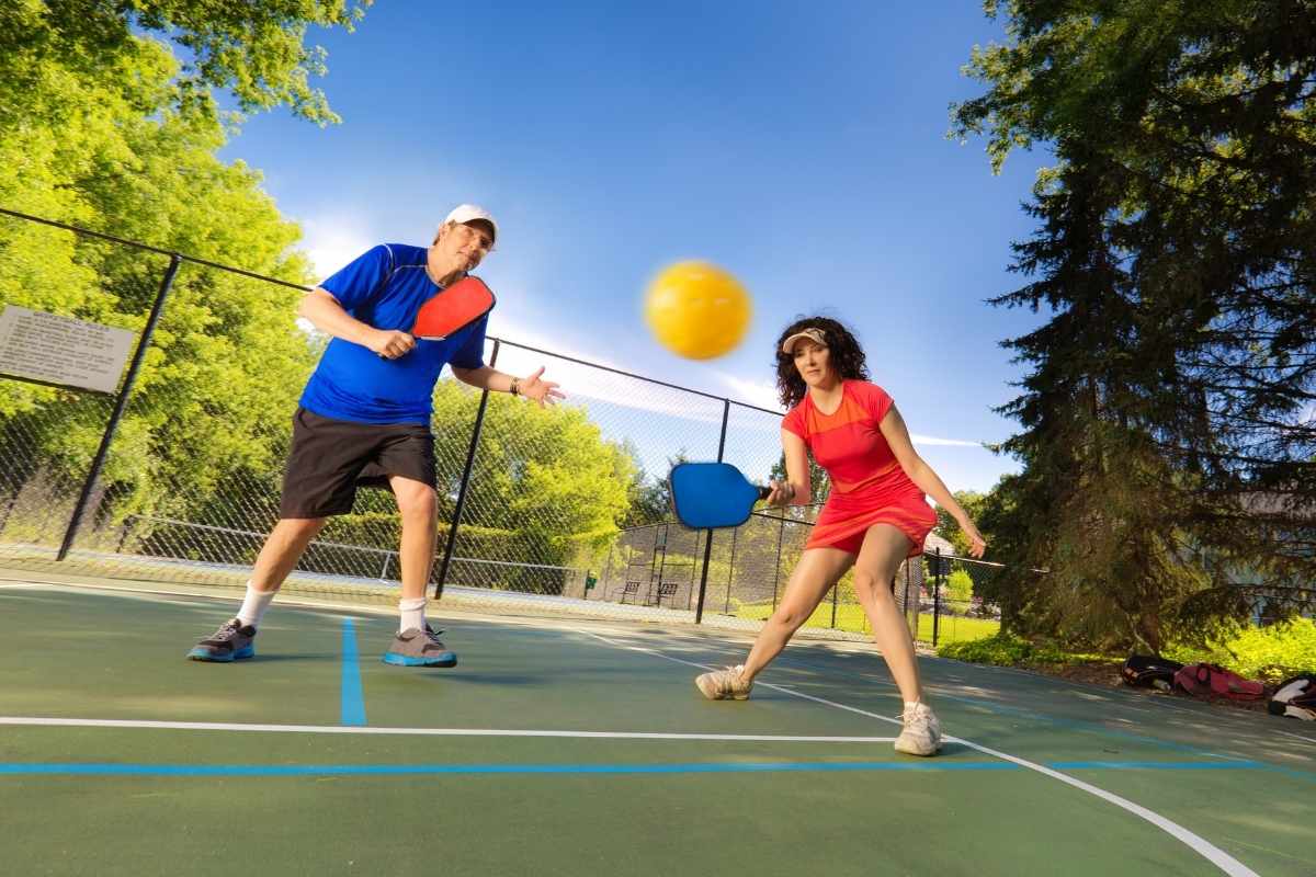 Adult man and woman playing pickleball in court.